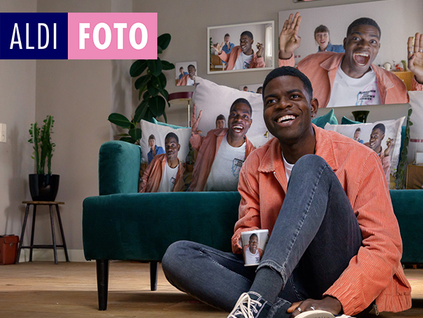 Mann sitzt vor Couch mit personalisierten Fotokissen.