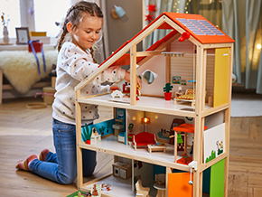 Mädchen spielt mit Holz-Puppenhaus im Kinderzimmer.